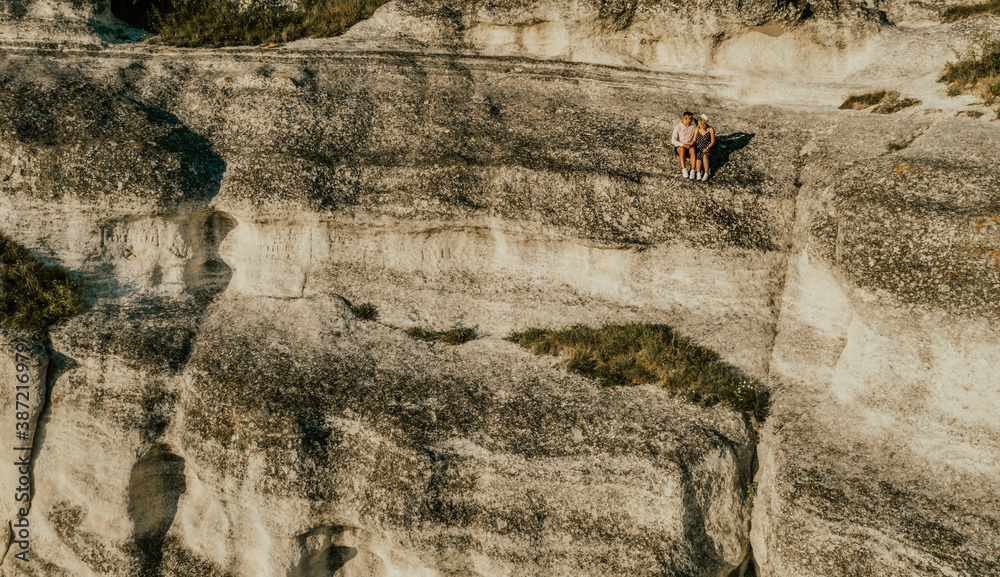 A man and woman in hat are sitting on large stone rock. A couple of fair-haired fair-skinned people in love are resting in nature in field at sunset. A man and woman in hat are sitting on large stone rock. A couple of fair-haired fair-skinned people in love are resting in nature in field at sunset.