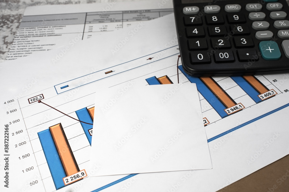 financial documents with a chart are on the desktop. A note sheet with a calculator lies on the documents financial documents with a chart are on the desktop. A note sheet with a calculator lies on the documents