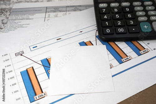 financial documents with a chart are on the desktop. A note sheet with a calculator lies on the documents