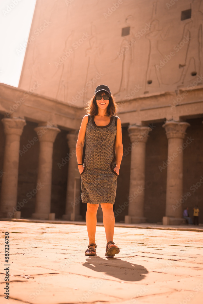 A young tourist wearing a cap visiting the Edfu Temple at sunrise in Aswan. Egypt, with the empty temple in the morning