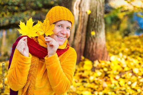 woman in her 50s standing in park in autumn and playing with leaves