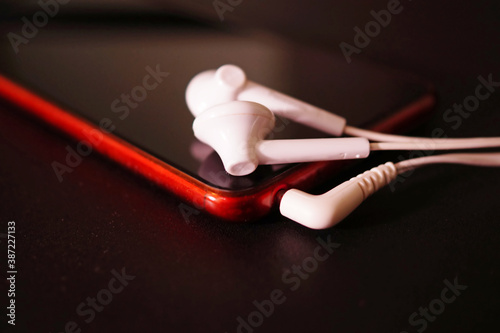Earphones on red smartphone close up.