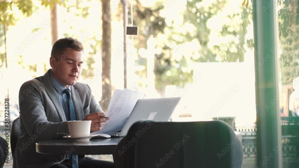 Distant view of a young businessman sitting at a table in a cafe using the laptop. Successful people, daily routine. Distant view of a young businessman sitting at a table in a cafe using the laptop. Successful people, daily routine.