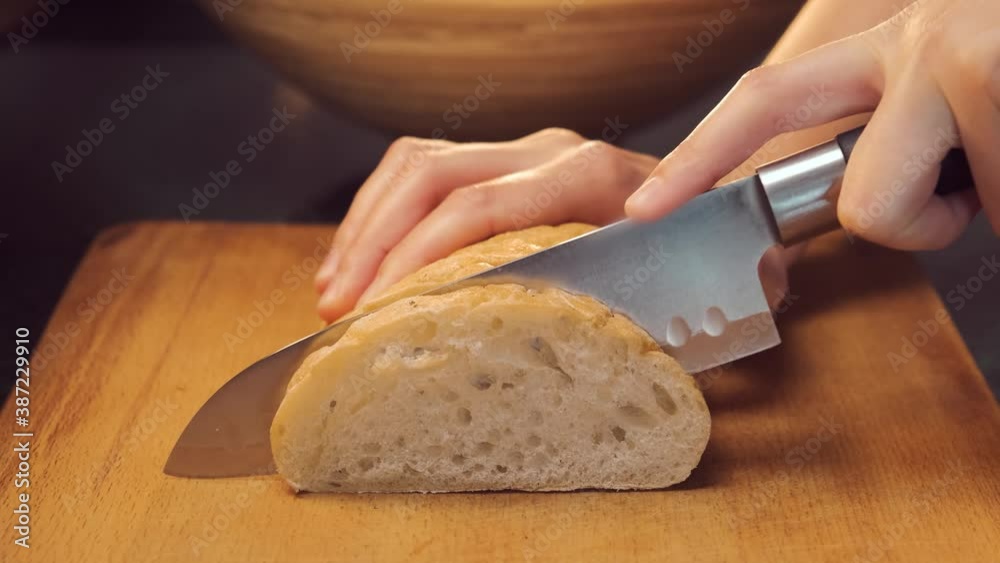 Woman slicing white bread. Female hands cutting bread with a knife on wooden board. Cooking process close up slow motion Woman slicing white bread. Female hands cutting bread with a knife on wooden board. Cooking process close up slow motion