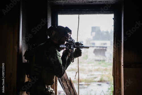 Soldier in full US MARSOC armed with assault rifle run through the abandoned building. Military clash. photo