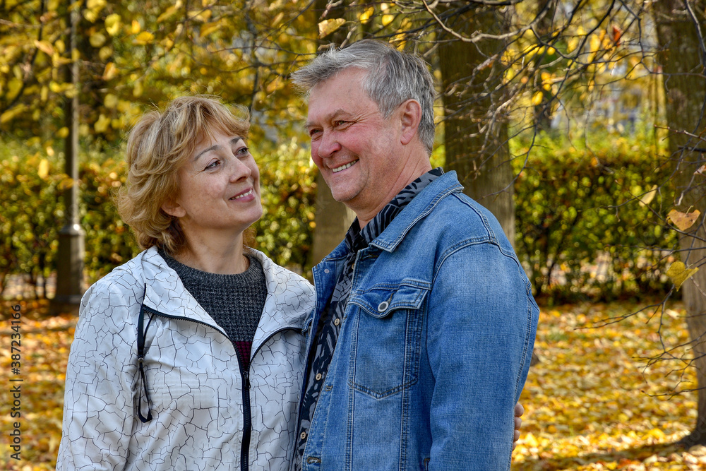 Happy, cheerful, smiling mature couple on a walk in the autumn city park. A woman in love looks tenderly at her husband.