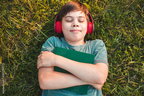 Young boy is  litening to the music, holing a planner lying on the grass photo
