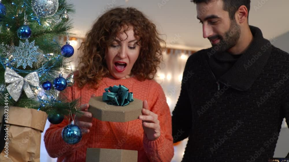 Couple enjoying and sharing presents by the Christmas tree in living room. Holidays preparation. Couple enjoying and sharing presents by the Christmas tree in living room. Holidays preparation.
