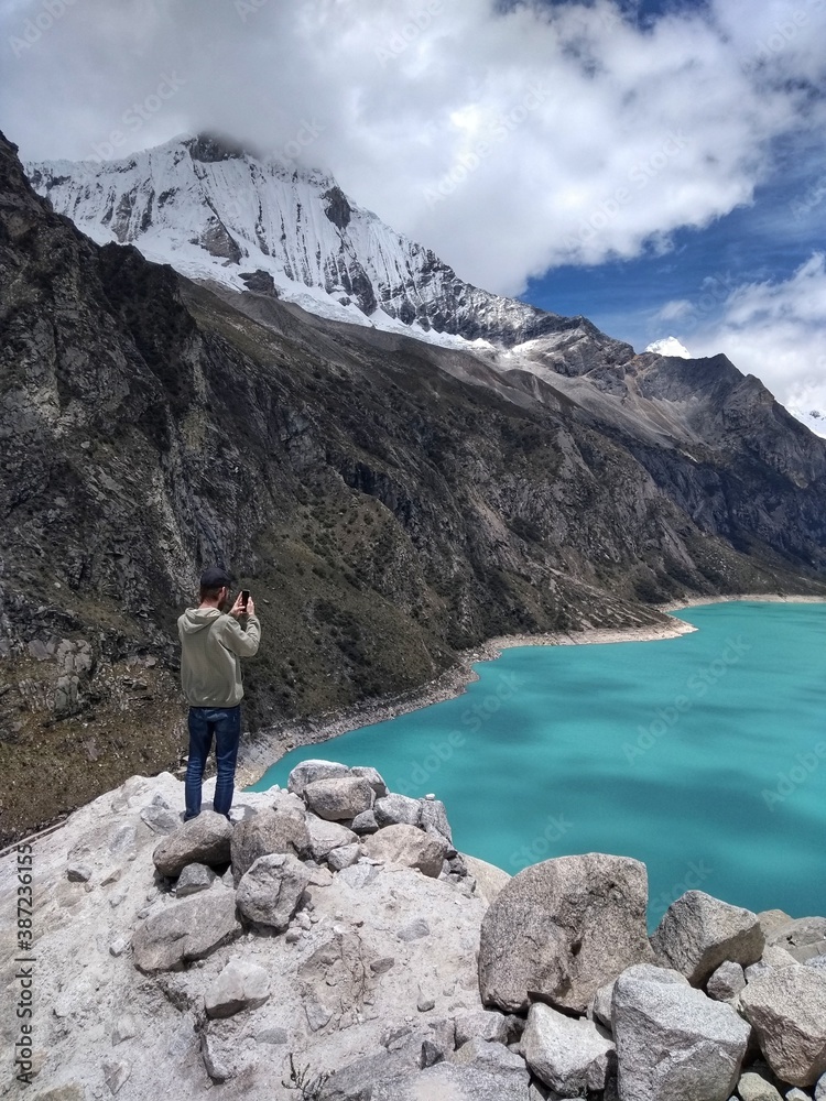 Man at Laguna Paron, Huaraz, Peru. A blue-green lake in the Cordillera Blanca on the Peruvian Andes. At 4185 meters above sea level, it's surrounded by snowy peaks and a pyramid mountain. 