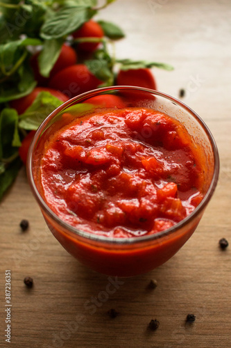 Tomato sauce for pasta or pizza in a glass bowl on a wooden background. Cooked with tomatoes, peppers, oil, garlic, tomato paste, oregano, onion and basil.Traditional Neapolitan recipe.