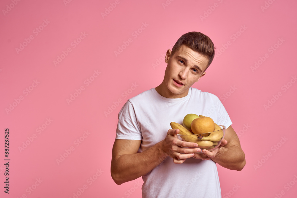 Man with fruits in hands on a pink background healthy food vitamins pink background white t-shirt model Man with fruits in hands on a pink background healthy food vitamins pink background white t-shirt model