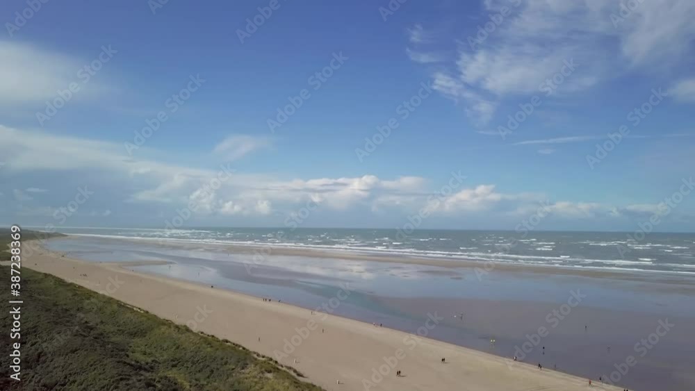 Drone flight to a wide beach in Ouddorp in the south of the Netherlands with some beach walkers. Zeeland. Windy nice weather with waves and interesting clouds in the distance. The camera moves up. 