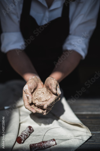 Wet hands covered with gray clay of potter holding raw piece of clay