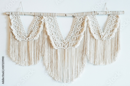 Boho style macrame wall panel made of natural cotton threads on a light wall. Concept of home decor in the style of Boho.