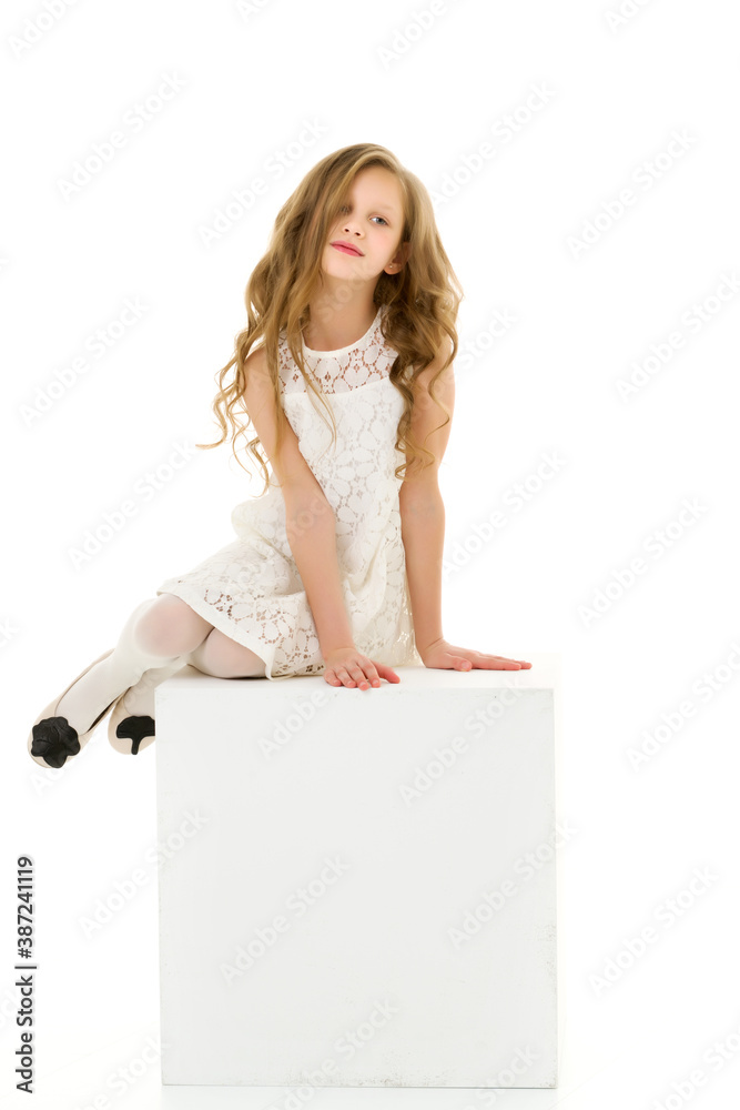 Beautiful Blonde Girl in White Dress Sitting on Cube on Her Knee. Beautiful Blonde Girl in White Dress Sitting on Cube on Her Knee.