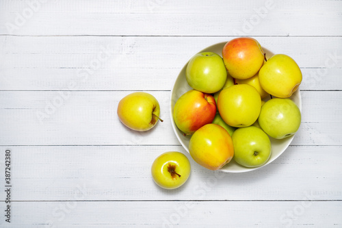 Yellow apples or golden apples on the plate on white wooden table. Top view. Copy space.