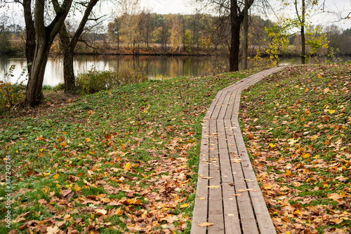 Autumn landscape. Winding wooden path leading to the river in the autumn park with fallen yellow leaves.