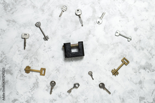 Lock and variety of keys on grey concrete background.