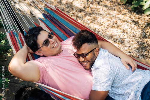 Gay couple snuggling and laughing together in hammock in back yard