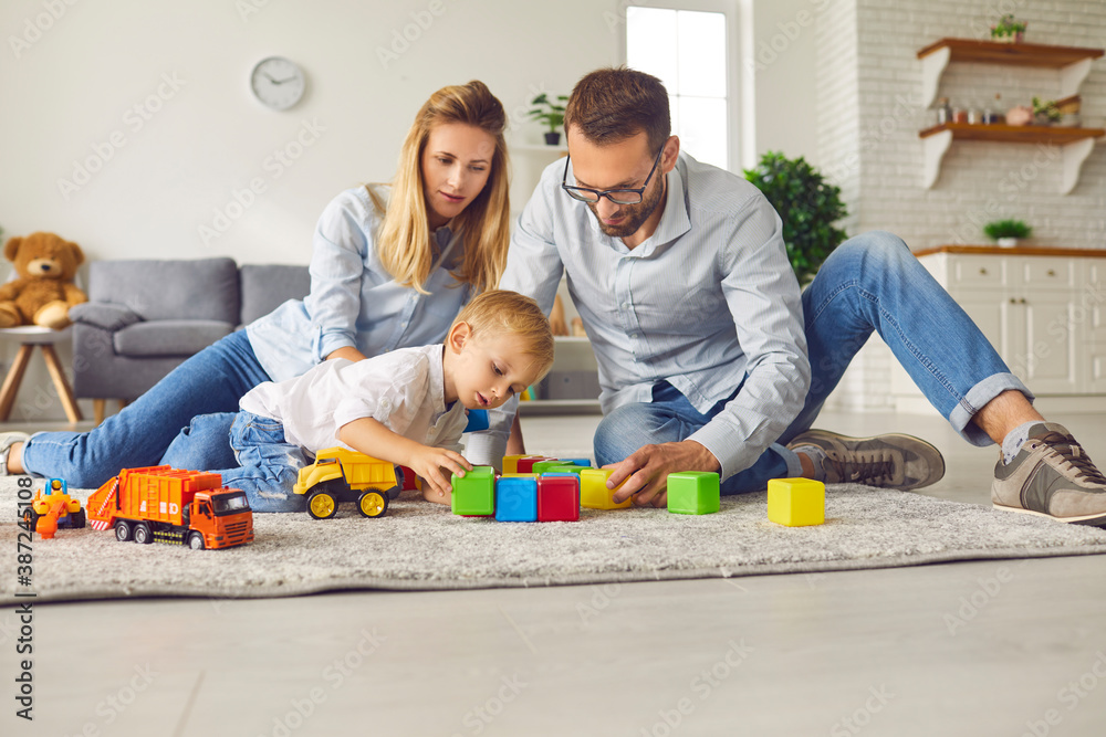© Studio Romantic - Concerned little boy makes colored cubes with his parents sitting on the carpet in the room. © Studio Romantic - Concerned little boy makes colored cubes with his parents sitting on the carpet in the room.