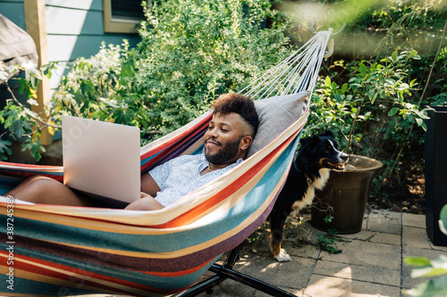 Man relaxing in hammock working on laptop computer 