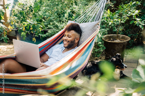 Man relaxing in hammock working on laptop computer  photo