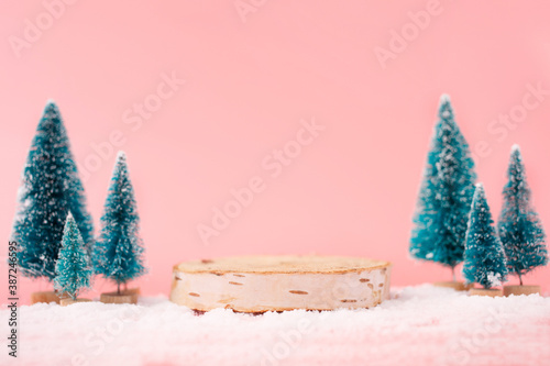 Mock up with wooden podium from a circle of wood on trendy pastel pink background with christmas decoration tree. Place for christmas product presentation