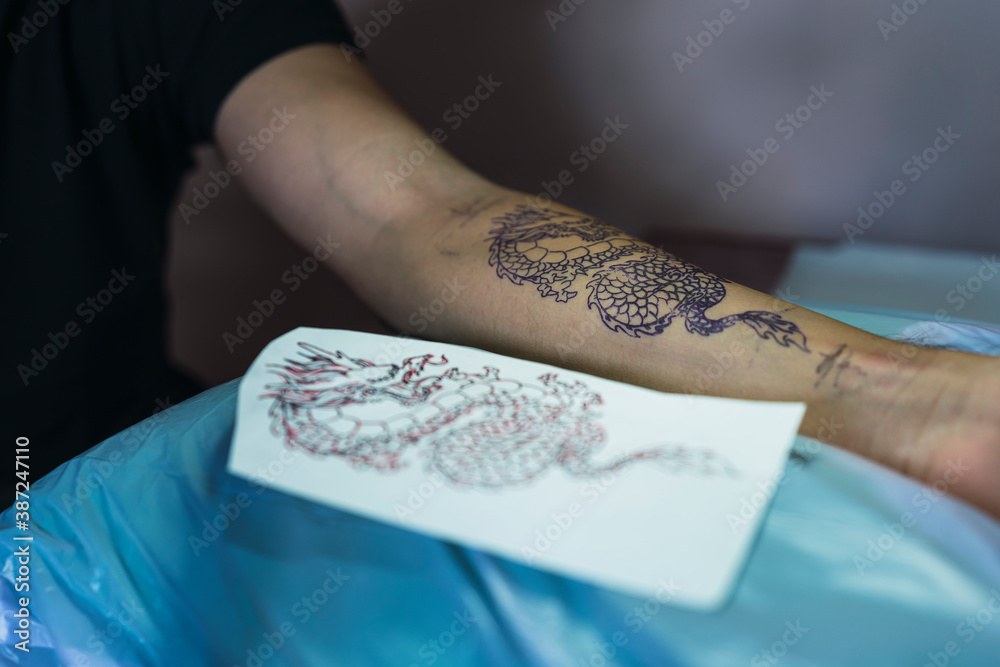 Chica joven con gafas tatuando a chico joven un dragon en el brazo