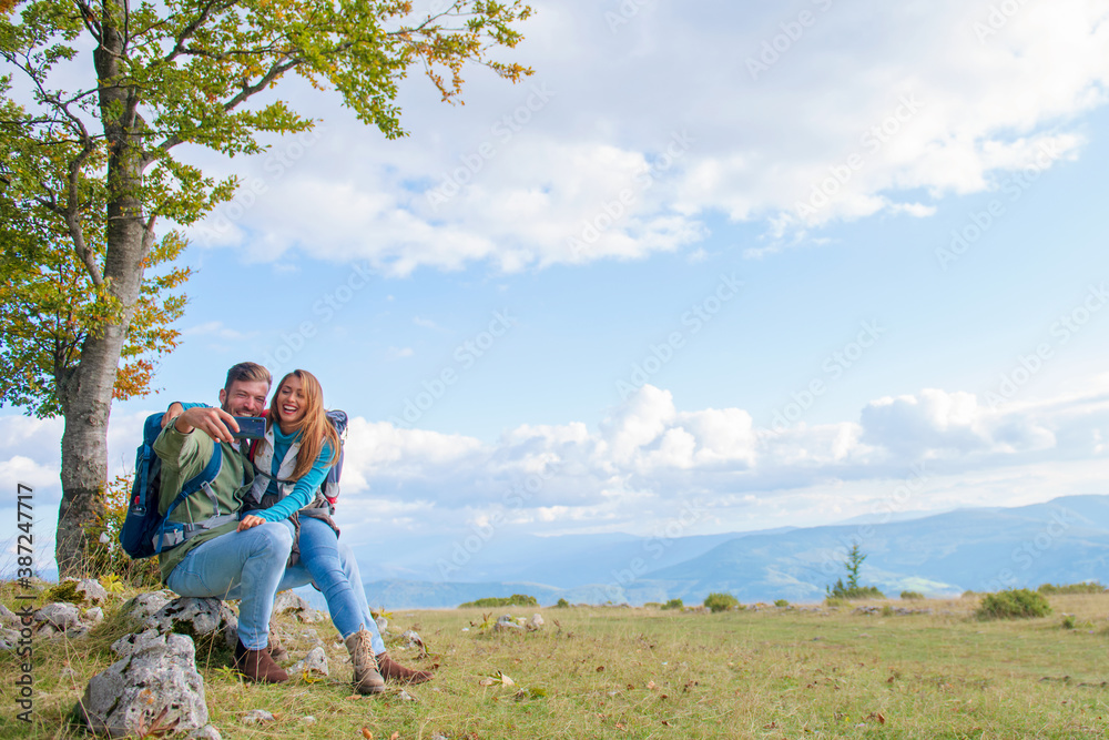 Couple Sitting On A Rock Resting During Hike and taking selfie Couple Sitting On A Rock Resting During Hike and taking selfie