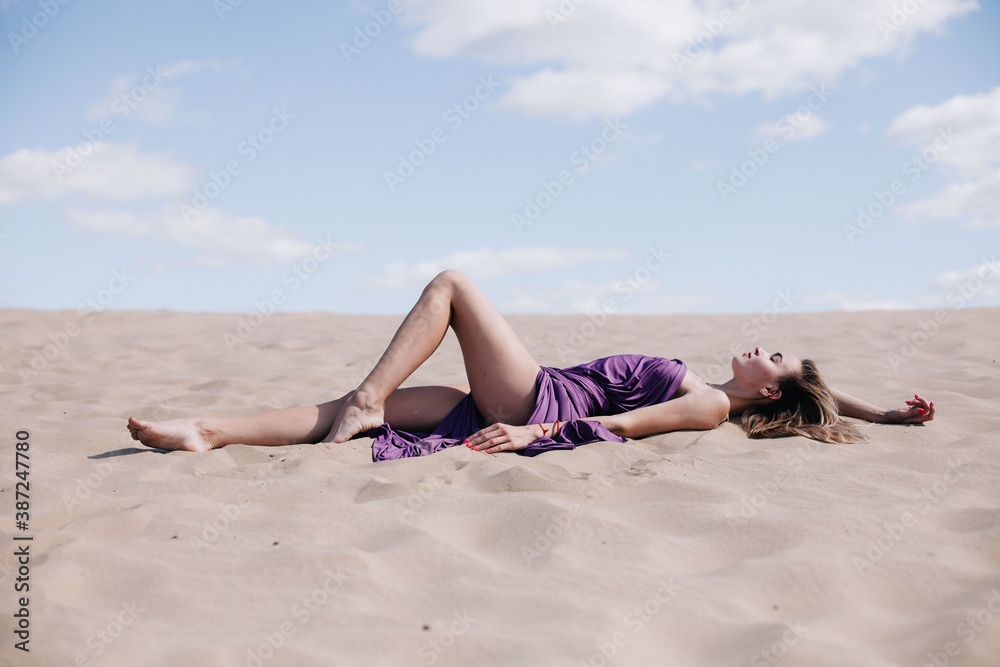 Young, slender girl with purple cloth poses in the desert