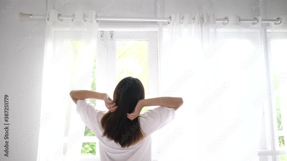 Young woman opening curtain of window and stretching arm Young woman opening curtain of window and stretching arm