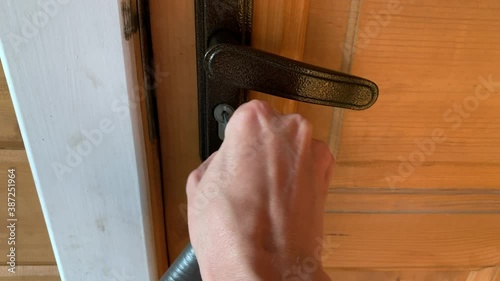 A hand holding a key and inserting it in a keyhole, unlocking and opening a white wooden door, home security and protection concept
