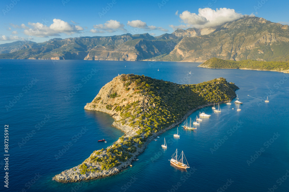 aerial view to island in sun light with yachts under blue sky and clouds on the tops - obrazy, fototapety, plakaty 