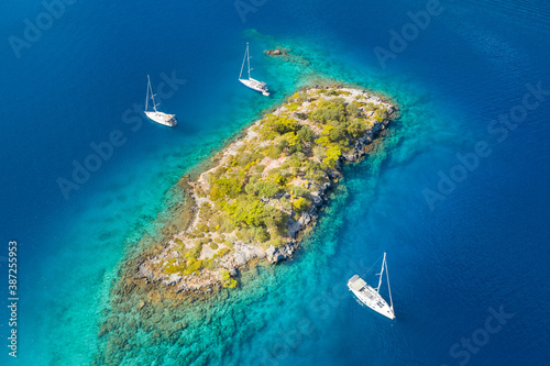 aerial view to little island in emerald water between three sailing yachts © sergejson