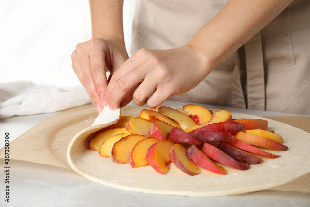 Woman making peach pie at kitchen table, closeup - obrazy, fototapety, plakaty 