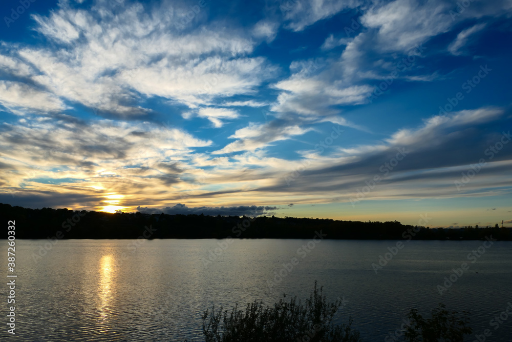 Amazing sunset over the water. Beautiful landscape with a lake and dramatic sky with cumulus clouds on the horizon.