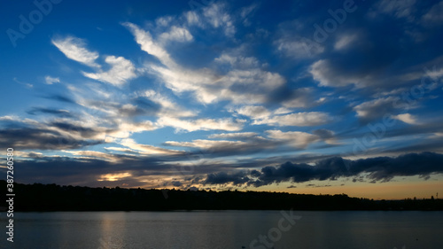 Amazing sunset over the water. Beautiful landscape with a lake and dramatic sky with cumulus clouds on the horizon.