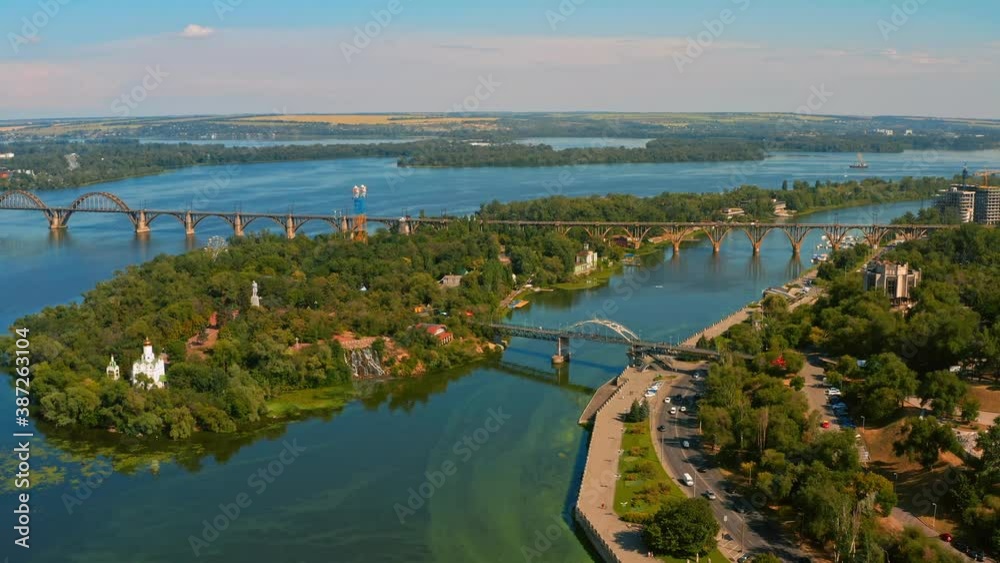Aerial view over beautiful urban environment with a wide river, long bridge, green landscape - while sunset. Drone flying above city landscape Aerial view over beautiful urban environment with a wide river, long bridge, green landscape - while sunset. Drone flying above city landscape