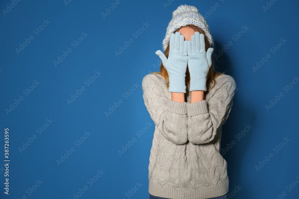 Woman wearing warm sweater, knitted hat and mittens on blue background. Space for text