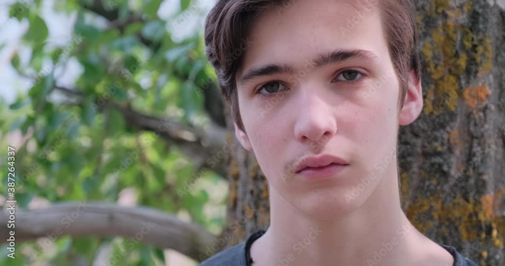 Young sad man looks on the camera. Unhappy alone young teenager, outdoors. Closeup face of handsome guy with sad eyes, on the nature. Closeup frustrated teenager face, outside Young sad man looks on the camera. Unhappy alone young teenager, outdoors. Closeup face of handsome guy with sad eyes, on the nature. Closeup frustrated teenager face, outside