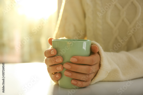 Woman holding elegant cup at table indoors, closeup