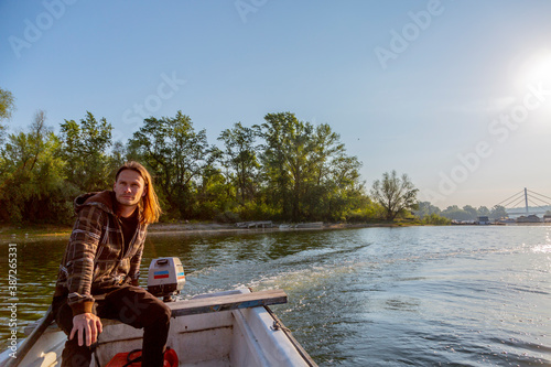 Sad man is riding a boat over river in sunset © MexChriss