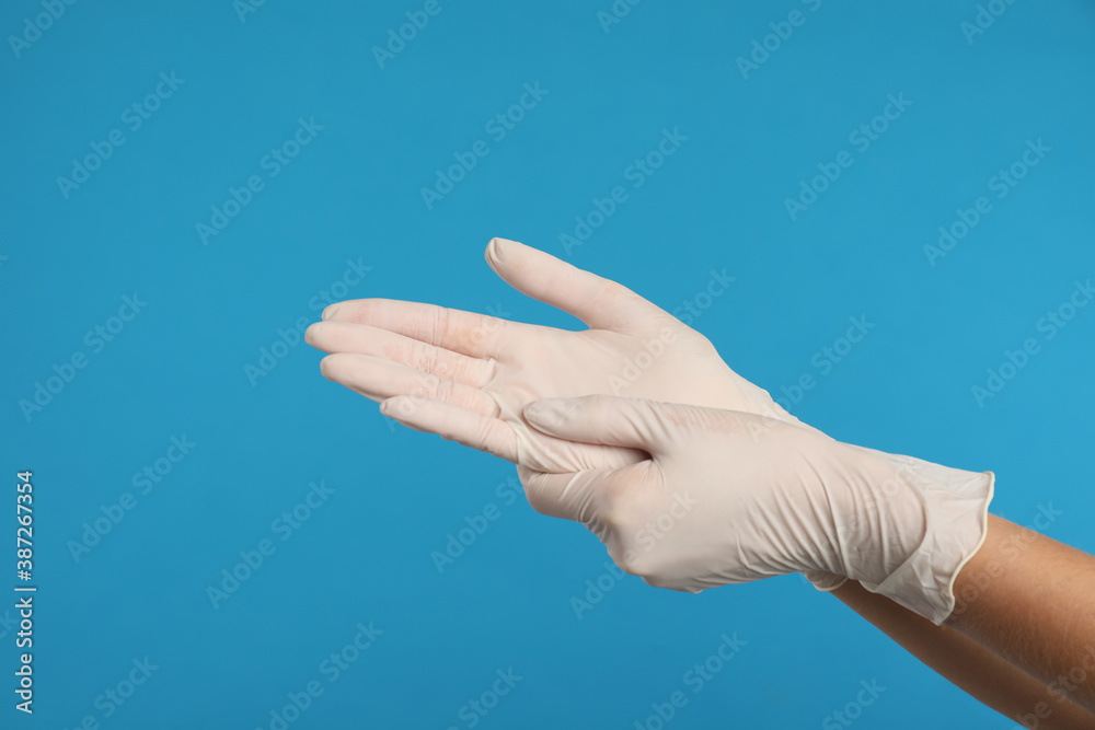 Doctor wearing medical gloves on light blue background, closeup Doctor wearing medical gloves on light blue background, closeup