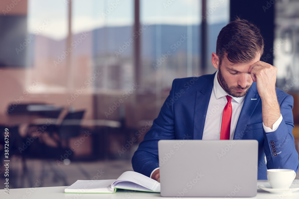 Feeling exhausted. Frustrated young beard man keeping eyes closed while sitting at his working place in office Feeling exhausted. Frustrated young beard man keeping eyes closed while sitting at his working place in office
