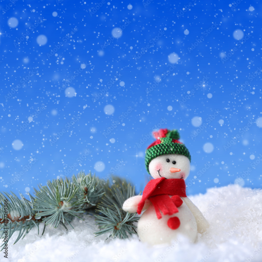 Cute snowman and fir tree branch on snow against blue background, bokeh effect