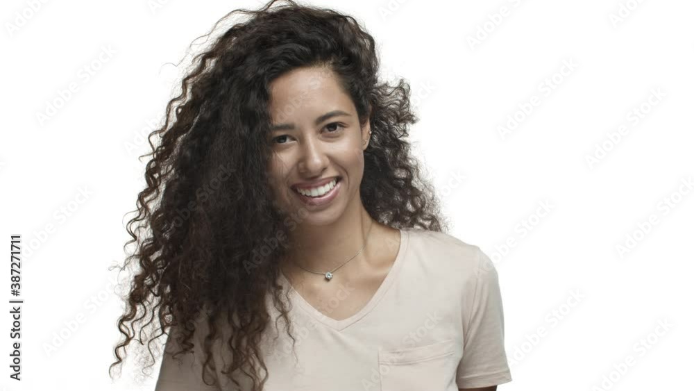 Close-up of pretty mexican woman with long curly hairstyle, dancing and smiling coquettish, celebrating good news, standing over white background Close-up of pretty mexican woman with long curly hairstyle, dancing and smiling coquettish, celebrating good news, standing over white background