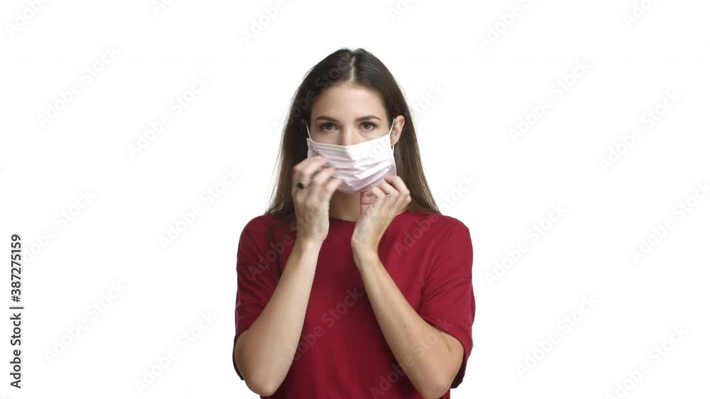 Coronavirus, social distancing and pandemic concept. Attractive brunette woman in red t-shirt put on medical mask in order to prevent catching covid-19, standing over white background Coronavirus, social distancing and pandemic concept. Attractive brunette woman in red t-shirt put on medical mask in order to prevent catching covid-19, standing over white background