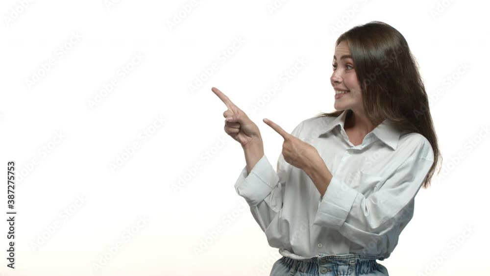 Video of attractive young woman in white shirt looking impressed, smiling and pointing fingers left at advertisement, nodding in approval, recommending something good Video of attractive young woman in white shirt looking impressed, smiling and pointing fingers left at advertisement, nodding in approval, recommending something good