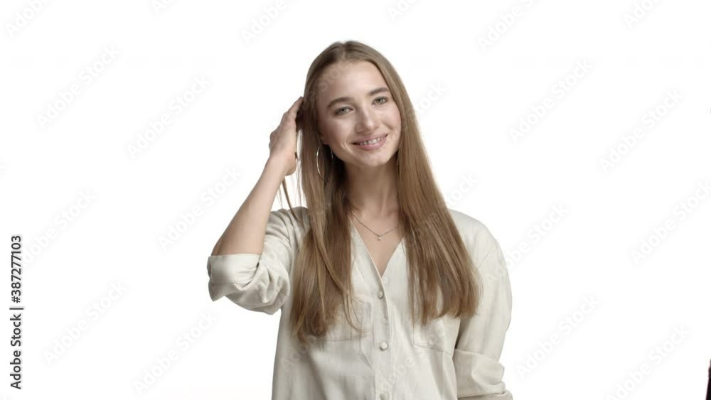 Lovely blond woman with braces on teeth, smiling flirty and touching hair coquettish, standing silly against white background in beige blouse Lovely blond woman with braces on teeth, smiling flirty and touching hair coquettish, standing silly against white background in beige blouse