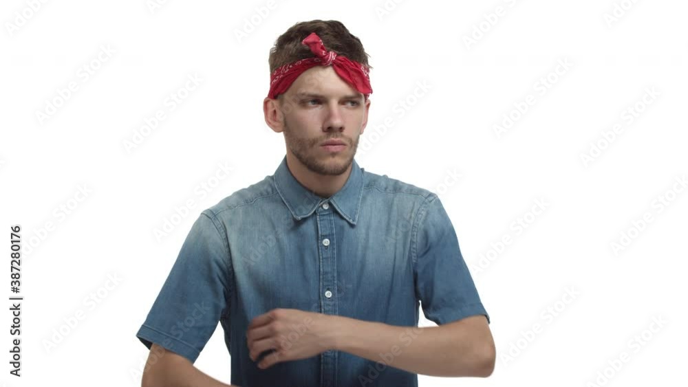 Young gloomy guy with red bandana, looking upset, sighing and crossing arms over chest, standing uneasy against white background Young gloomy guy with red bandana, looking upset, sighing and crossing arms over chest, standing uneasy against white background